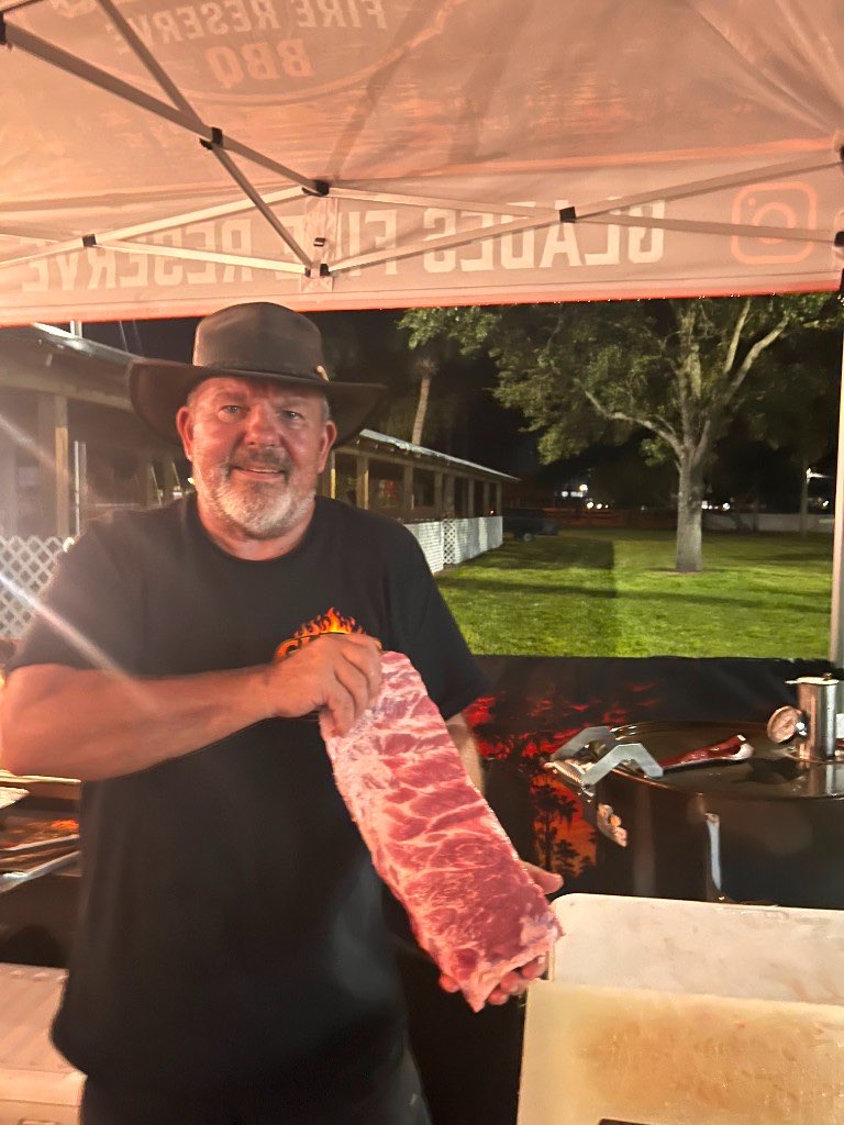 Pitmaster holding up a fresh rack of ribs at the tent after dark