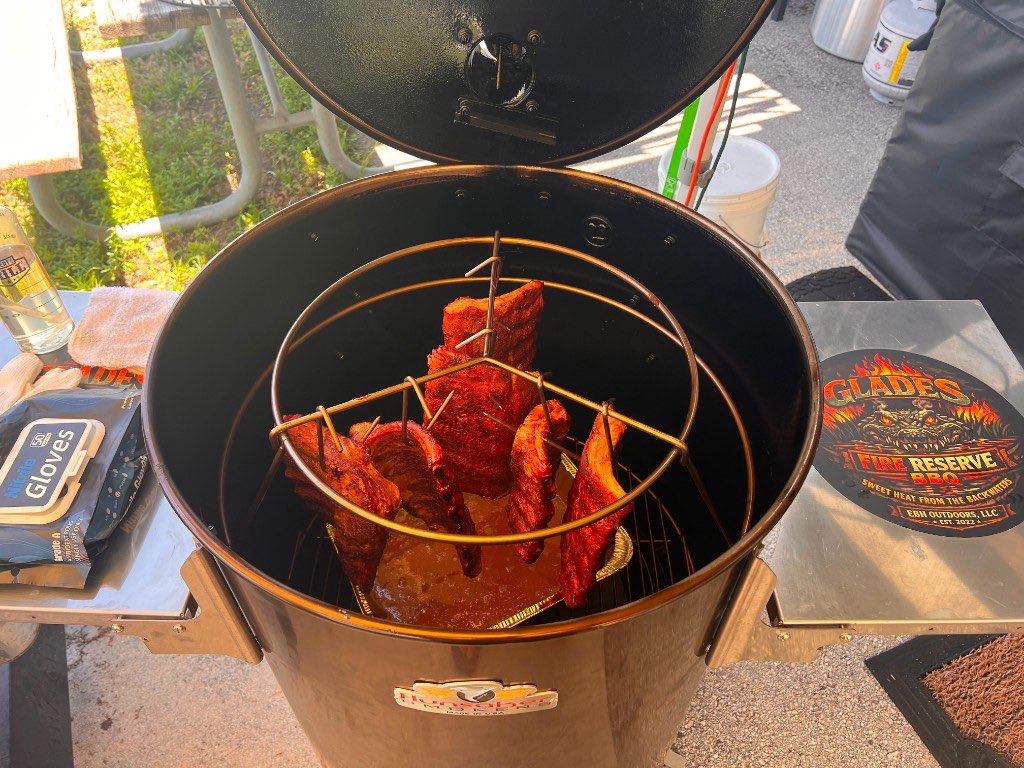 Racks of ribs hanging from hooks inside an open drum smoker