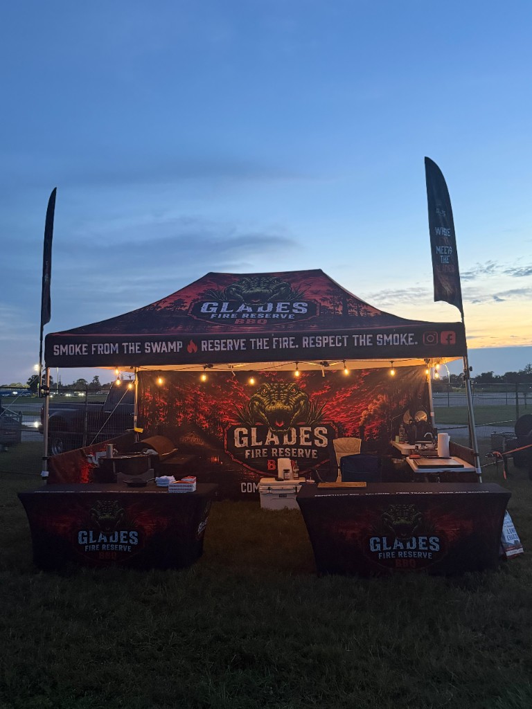 The Glades Fire Reserve canopy and skirted tables glowing under string lights at dusk on the competition grounds