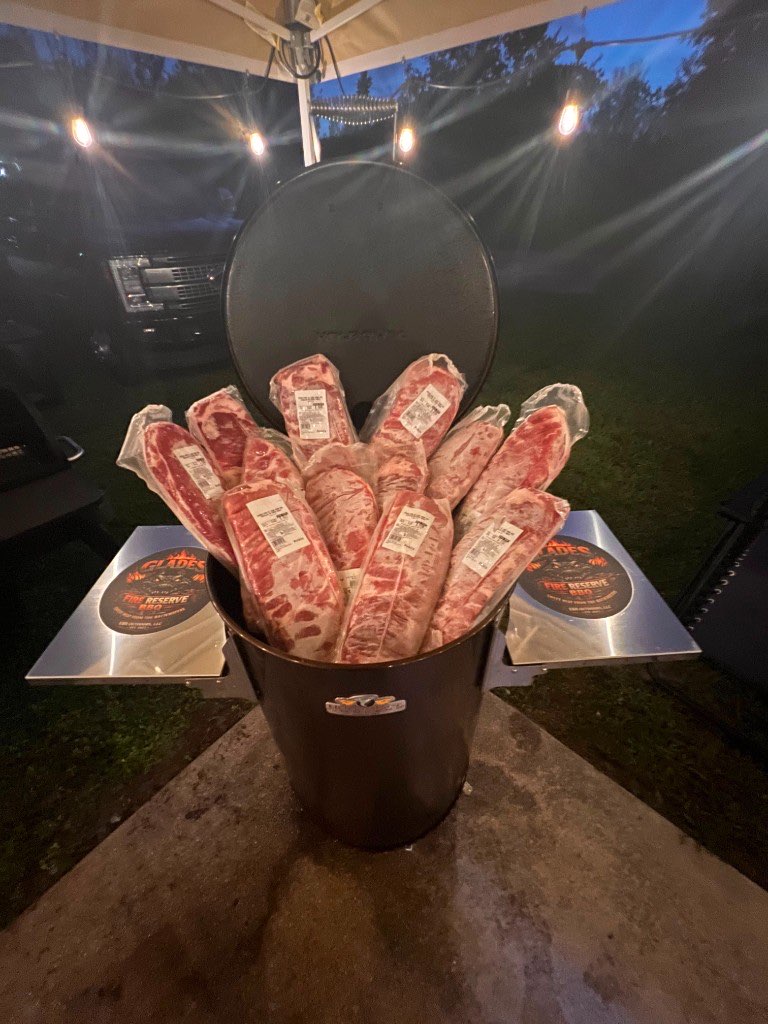 A drum smoker packed with racks of ribs at night under string lights