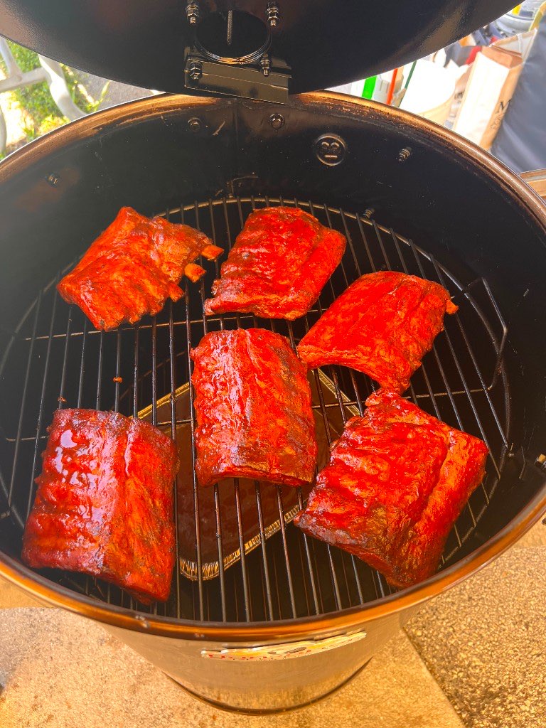 Six rubbed racks of ribs laid out on the grate of the drum smoker