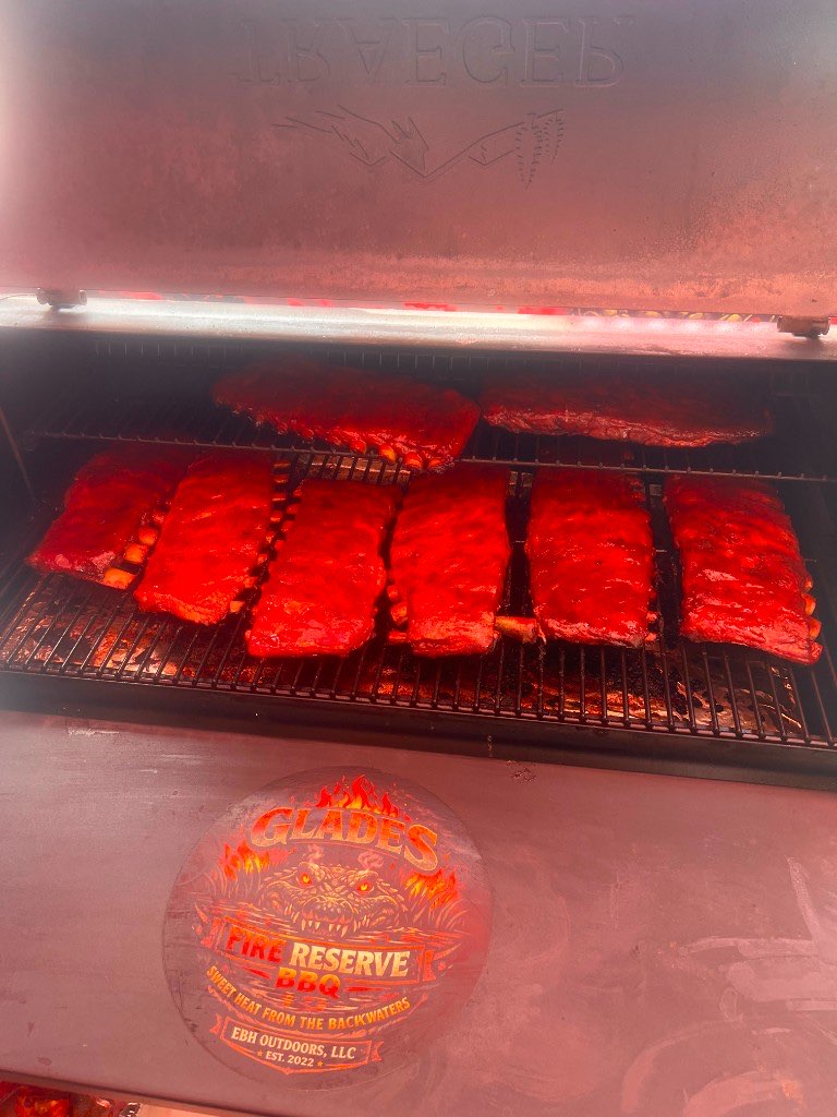 Six glazed racks of ribs glowing under the lid of the smoker, above the Glades Fire Reserve gator crest