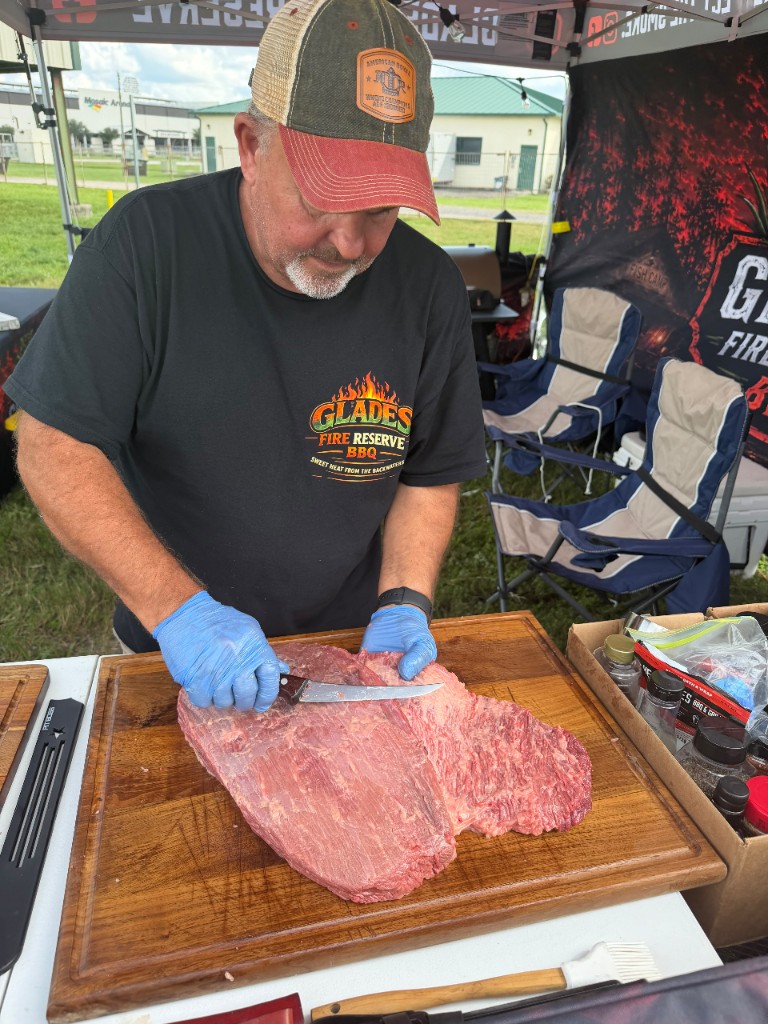 Gloved hands trimming a raw brisket with a boning knife at the competition tent