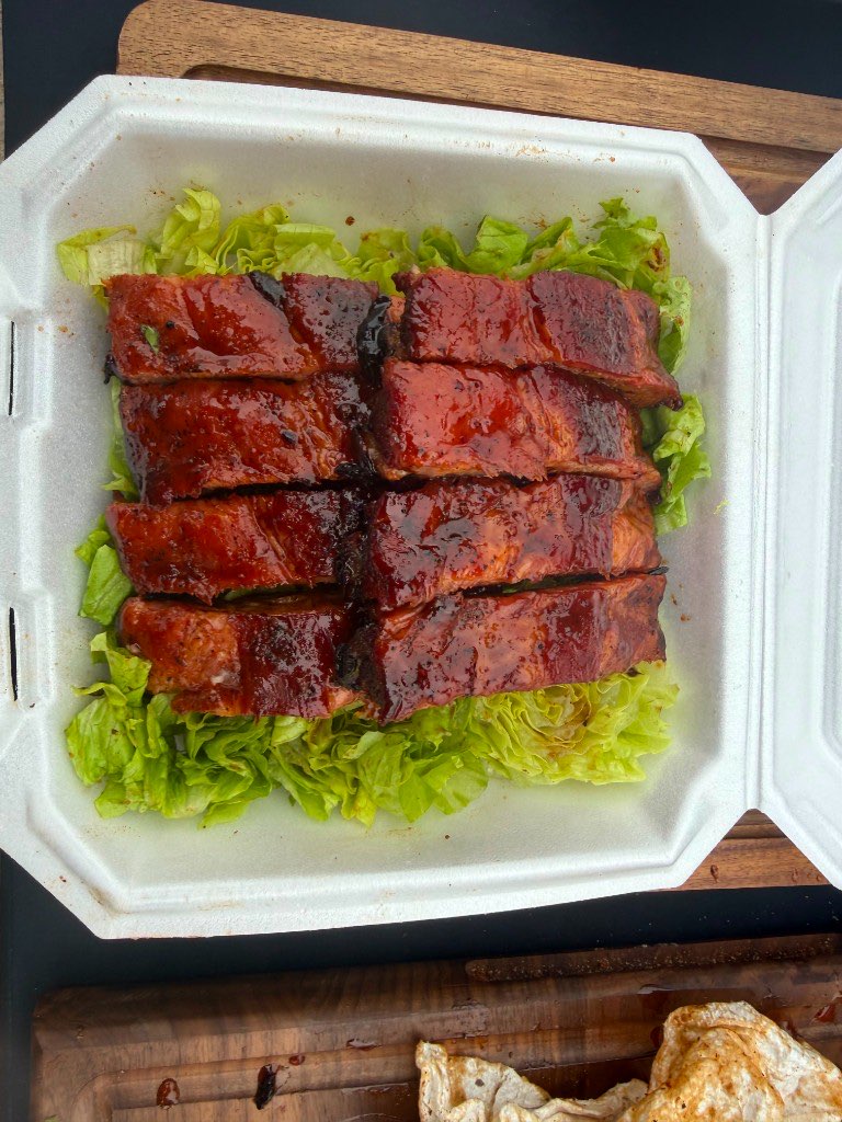 Eight glazed rib bones lined up on a bed of shredded lettuce in a competition turn-in box
