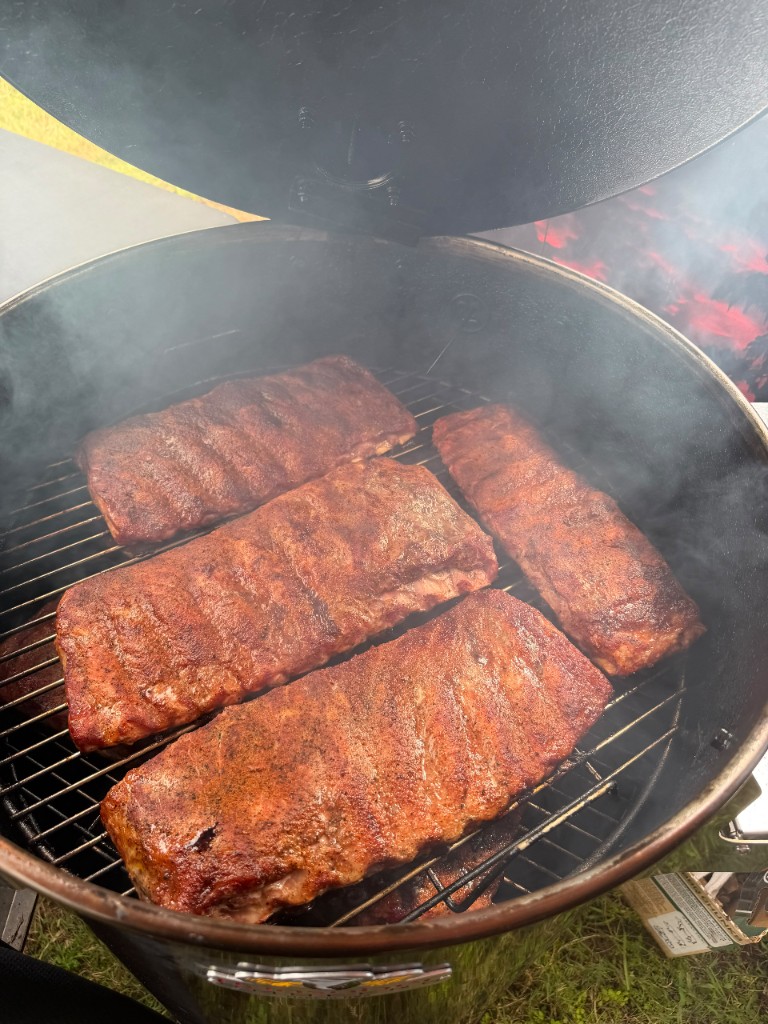 Five racks of ribs with a deep mahogany bark wrapped in smoke inside the open drum