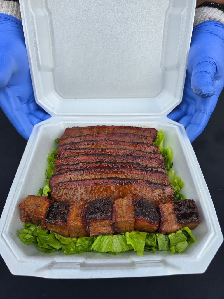 Close-up of the brisket turn-in box: glazed slices fanned over a row of burnt ends on a bed of lettuce